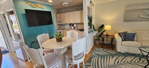A modern kitchen with white cabinets, a flat-screen TV, and a dining area with a round table and chairs. - Paradise on the Point: Mermaid suite, Steps from the Beach, & Harbor. (Destin)