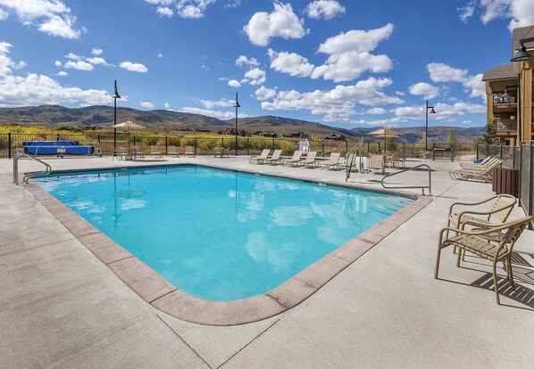 Piscina rectangular con agua cristalina y azul, rodeada de sillas de descanso y una terraza de hormigón.