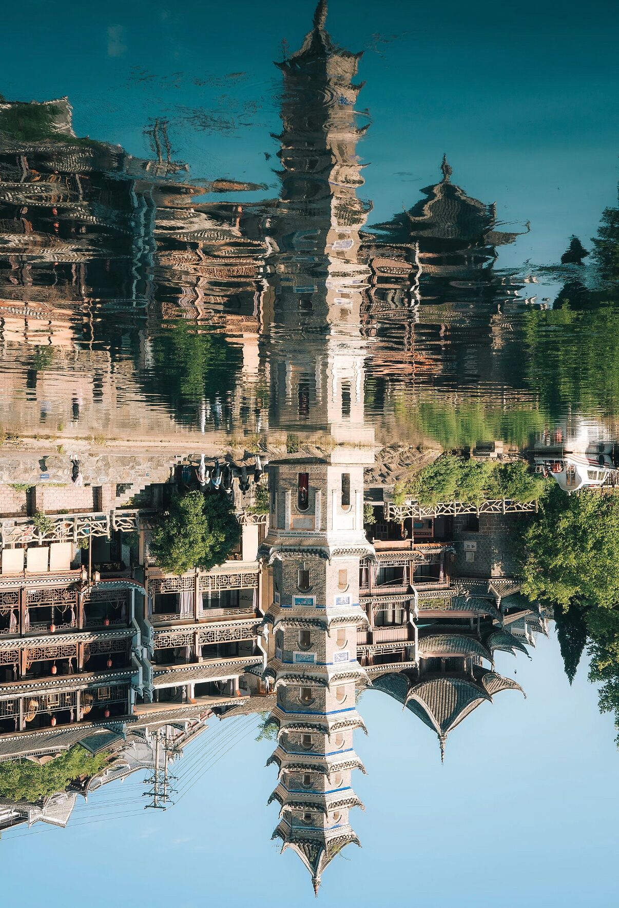 A traditional multi-tiered pagoda reflected in calm water, surrounded by traditional architecture and greenery.
