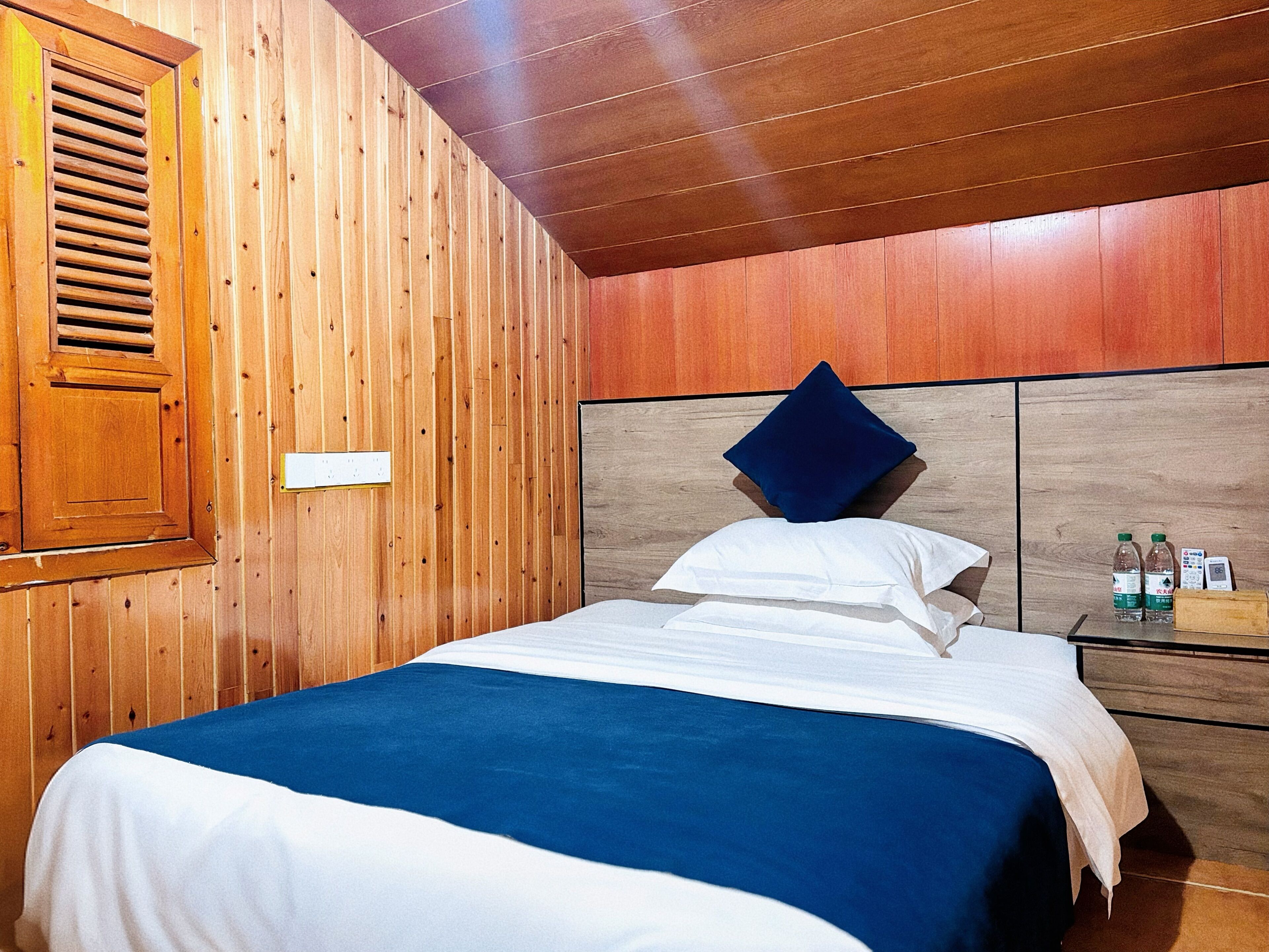 A wooden-paneled room with a bed, a nightstand with water bottles, and a wooden headboard.