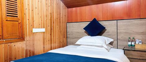 A wooden-paneled room with a bed, a nightstand with water bottles, and a wooden headboard.