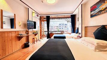 Habitación de hotel con cama, televisor, ventana y vista a edificios, además de piso de madera.