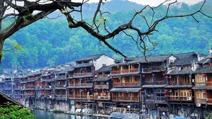 Traditional wooden buildings with multiple stories, some with balconies, situated along a river. - Fenghuang Meomory Riverview Inn (Xiangxi)
