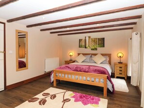 Een slaapkamer met een houten bed, twee nachtkastjes met lampen, een radiator, een spiegel en een muur met drie ingekaderde afbeeldingen.