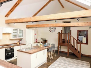 A kitchen with a wooden ceiling, a dining area with a wooden staircase, and a kitchen island. - Cider Press Cottage (Torpoint)