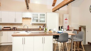 A modern kitchen with white cabinets, a wooden island, and a dining area with two chairs. - Cider Press Cottage (Torpoint)