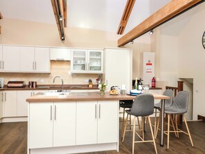 A modern kitchen with white cabinets, a wooden island, and a dining area with two chairs. - Cider Press Cottage (Torpoint)