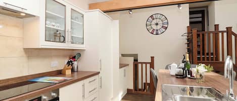 A kitchen with a built-in oven, a wooden countertop, a sink, and a clock on the wall.