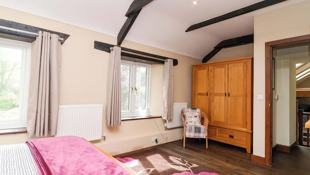 A bedroom with a bed, a wooden wardrobe, a radiator, and a window with curtains. - Cider Press Cottage (Torpoint)