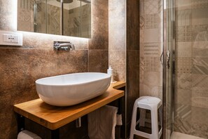 A bathroom with a large white vessel sink, a wooden countertop, a glass shower enclosure, and patterned tiles. - Pachita's Seaside Rooms - Polignano a Mare (Polignano a Mare)