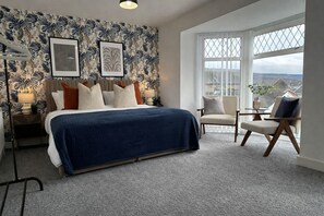 A bedroom with a bed, a chair, a nightstand, a lamp, and a window with a view.