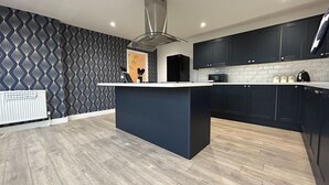Uma cozinha moderna com ilha central, armários escuros, micro-ondas e coifa.