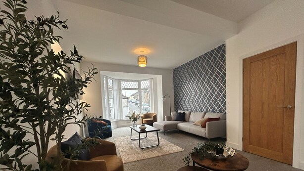 Uma sala de estar com sofá, poltronas, mesa de centro e uma planta.