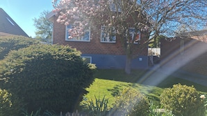 A residential building with a brick facade, a large tree with pink blossoms, and well-maintained lawns.