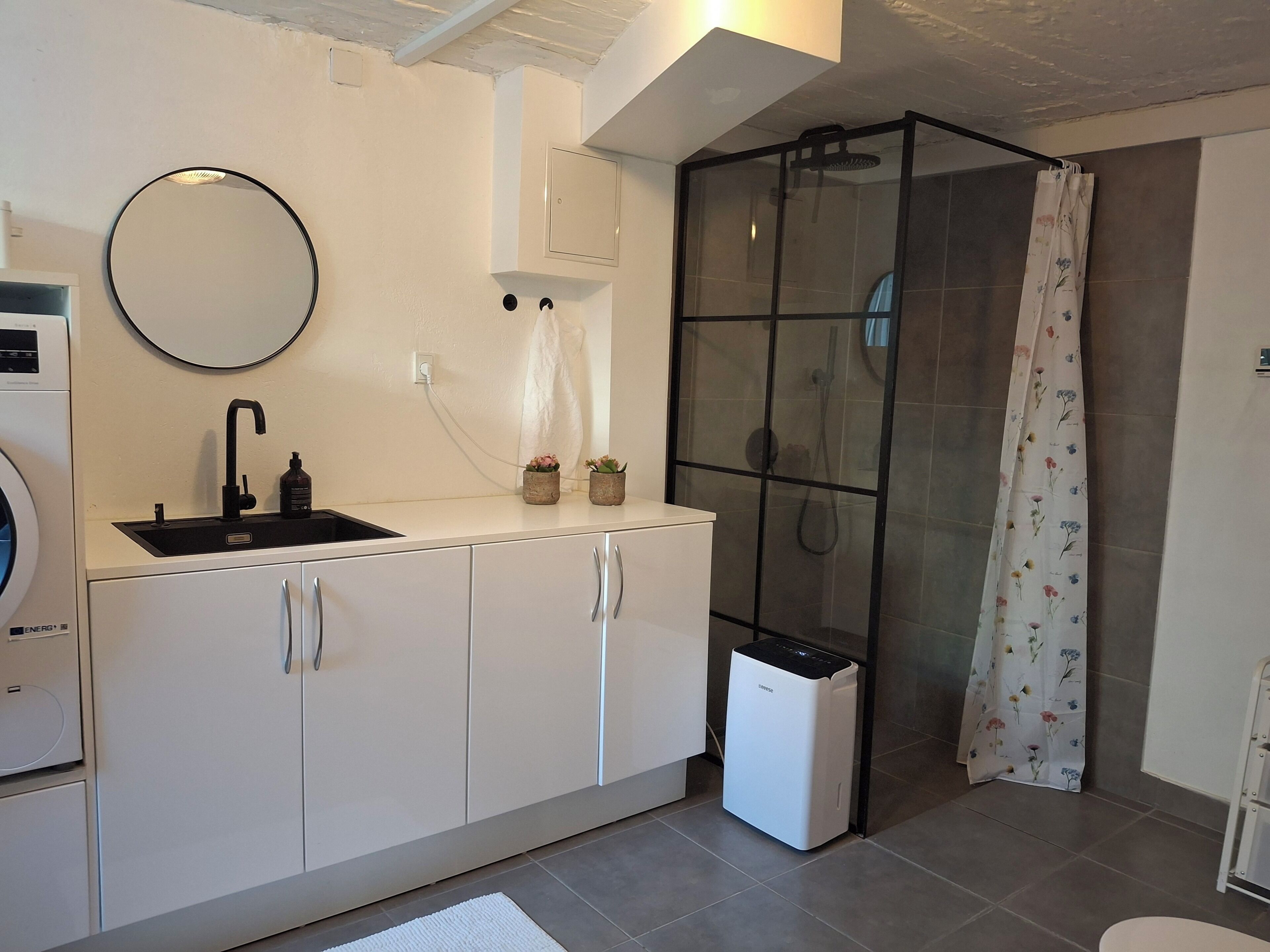 A compact kitchen with a sink, mirror, cabinets, and a small trash bin.