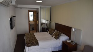 Una habitación de hotel con una cama, una mesita de noche, una silla, un espejo y una puerta que da a un baño.