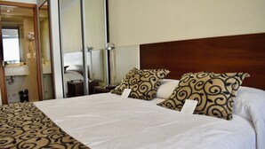 Habitación de hotel con una cama grande, dos almohadas estampadas, una mesita de noche, una lámpara y un espejo.