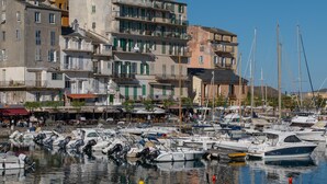 Puerto deportivo con barcos amarrados, un edificio con balcones y un cielo despejado.