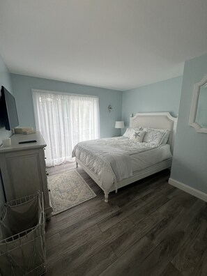A bedroom with a bed, a dresser, a lamp, and a window with curtains.