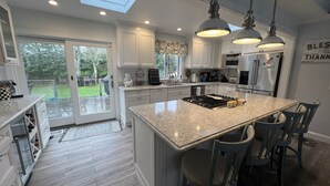 Una cucina moderna con una grande isola, mobili bianchi e illuminazione a sospensione.