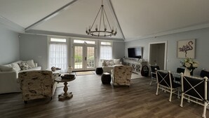 Un ampio soggiorno con soffitto alto, un lampadario, una televisione, una zona pranzo con tavolo e sedie e un'ampia finestra con tende.