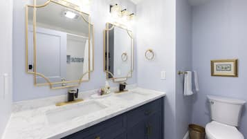 A bathroom with a white toilet, a sink with a gold faucet, and two large mirrors with gold frames.