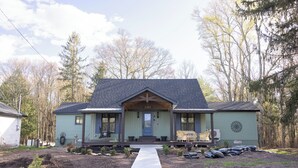 Une maison de plain-pied avec un porche à l’avant, une porte d’entrée bien visible et un petit jardin devant, avec un chemin en béton menant à la porte.