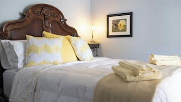 Una cama bien hecha con una colcha blanca y amarilla, un cabecero de madera y una lámpara de noche.