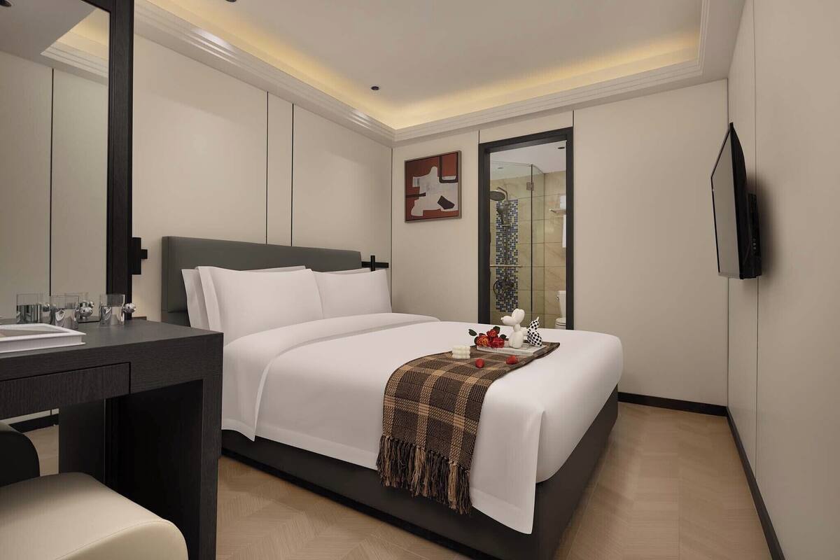 Ein modernes Hotelzimmer mit Bett, Nachttisch und einem an der Wand befestigten Fernseher.