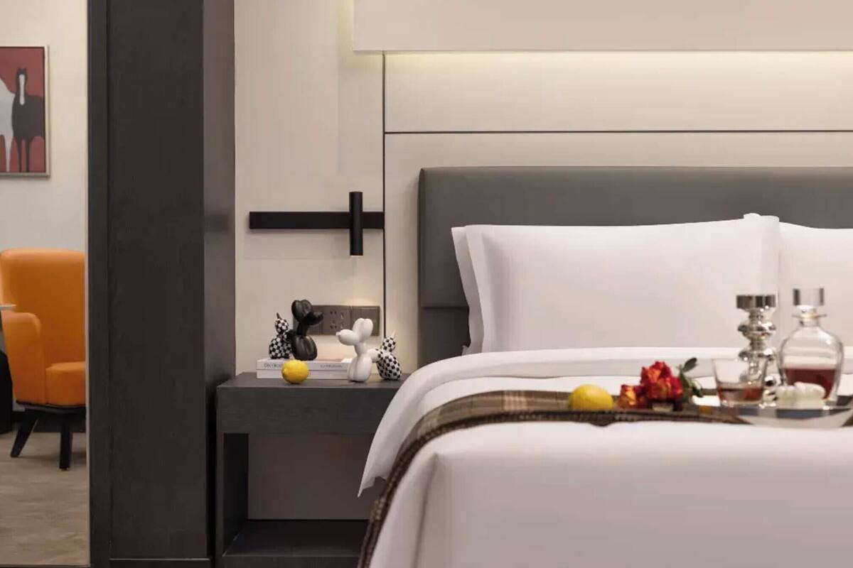 Ein Hotelzimmer mit Bett, Nachttisch, Stuhl und einem an der Wand hängenden Kunstwerk.
