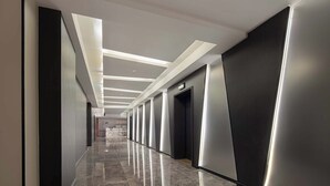 Een moderne hotelgang met een glanzende marmeren vloer, inbouwverlichting en een rij van liften.