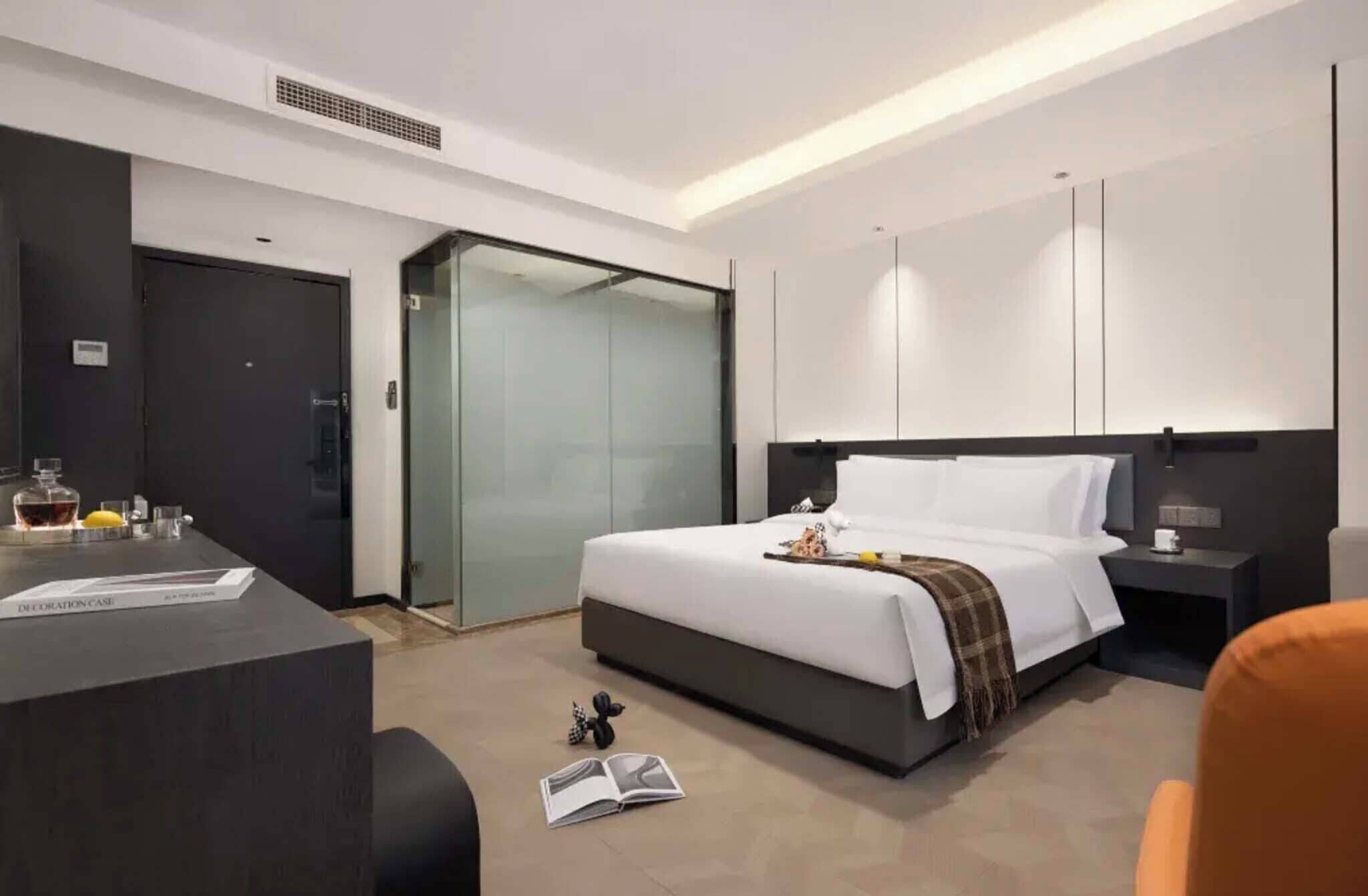 Moderni hotellihuone, jossa on sänky, yöpöytä ja työpöytä tuolilla.