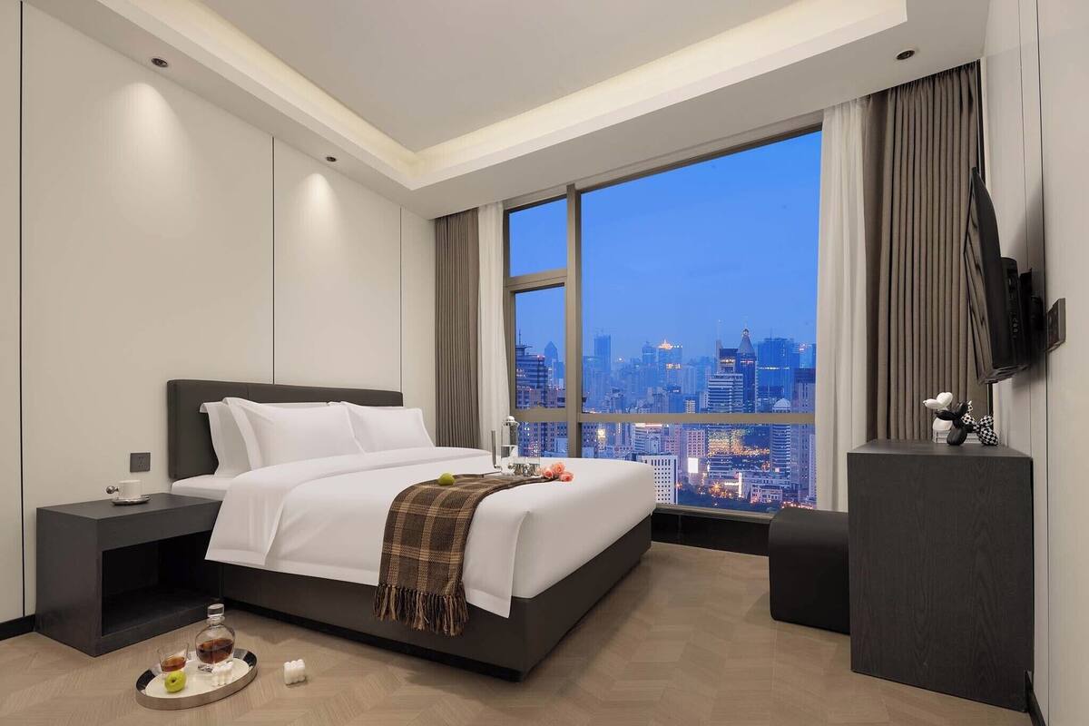Ein modernes Hotelzimmer mit einem großen Bett, einem Nachttisch, einem Flachbildfernseher und Blick auf die Stadt.