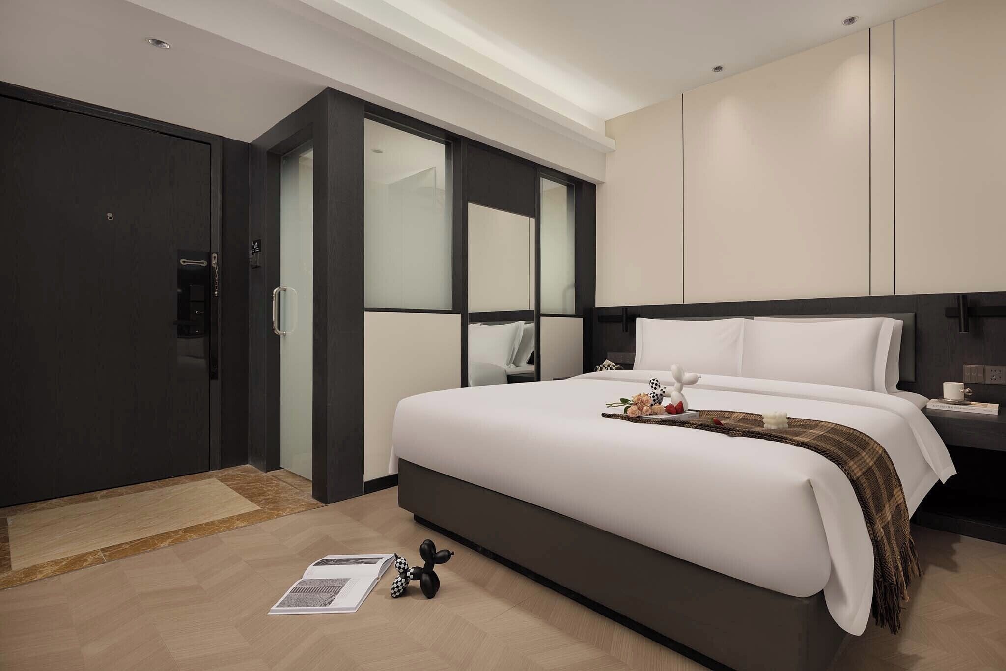 A modern hotel room with a large bed, a wardrobe, a mirror, and a bedside table.