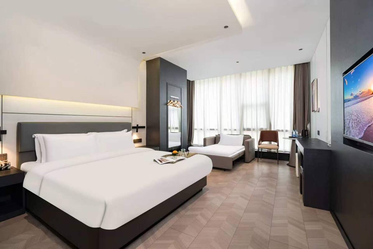 Ein modernes Hotelzimmer mit einem großen Bett, einer Couch, einem Fernseher und einem Schreibtisch.