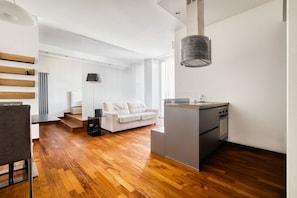 A modern kitchen with a central island, a dining area with a sofa, and a staircase leading to an upper level. - Hostmate - Milano - Viale Monza - NoLo (Milano)
