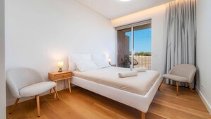 Een moderne slaapkamer met een bed, twee stoelen, een nachtkastje en een raam met gordijnen.
