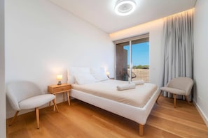 A modern bedroom with a bed, two chairs, a nightstand, and a window with curtains. - Horizon Smiles Beach Apartments (Loulé)