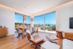 A modern living room with a dining area, large windows, and a view of the sea. - Horizon Smiles Beach Apartments (Loulé)
