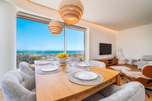 A dining area with a wooden table set for four, a Buddha statue, and a large window with a view of the sea. - Horizon Smiles Beach Apartments (Loulé)