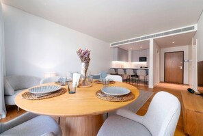 Ein moderner Essbereich mit einem runden Holztisch, grauen Polsterstühlen und einer Vase mit Blumen.