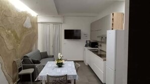A compact kitchen with a dining table, a sofa, and a TV mounted on the wall. - MEDUSA Residence B&B  (Margherita di Savoia)