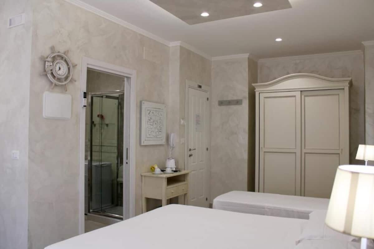 A hotel room with a bed, a desk with a lamp, a wardrobe, and a shower area.