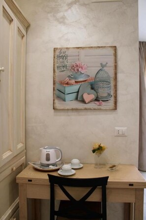 Un comedor con una mesa, sillas, un cuadro en la pared y un hervidor.