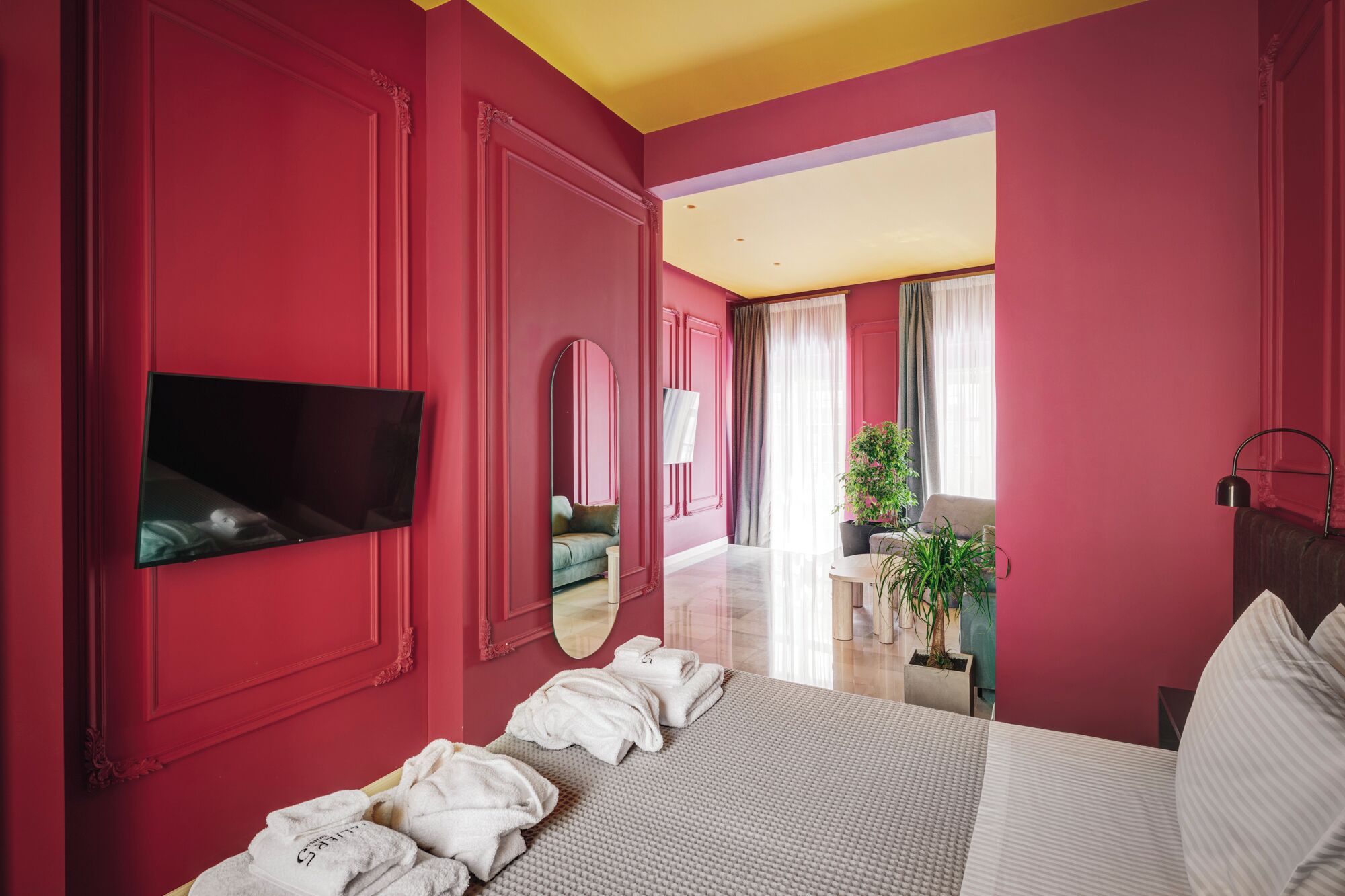 Habitación de hotel con cama, televisor, espejo, baño con planta y vista al exterior.