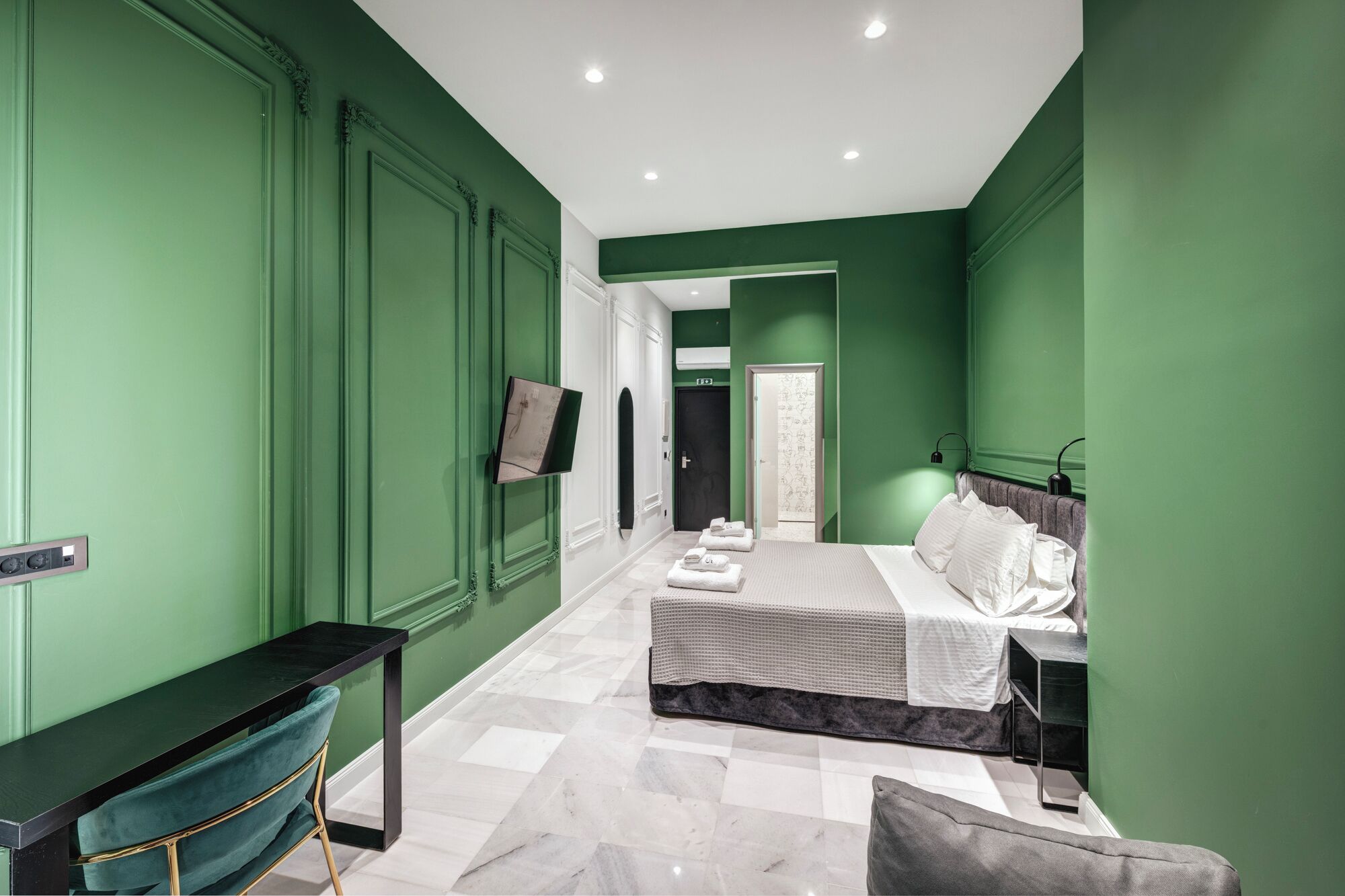 Una habitación de hotel con cama, mesita de noche y televisor montado en la pared.