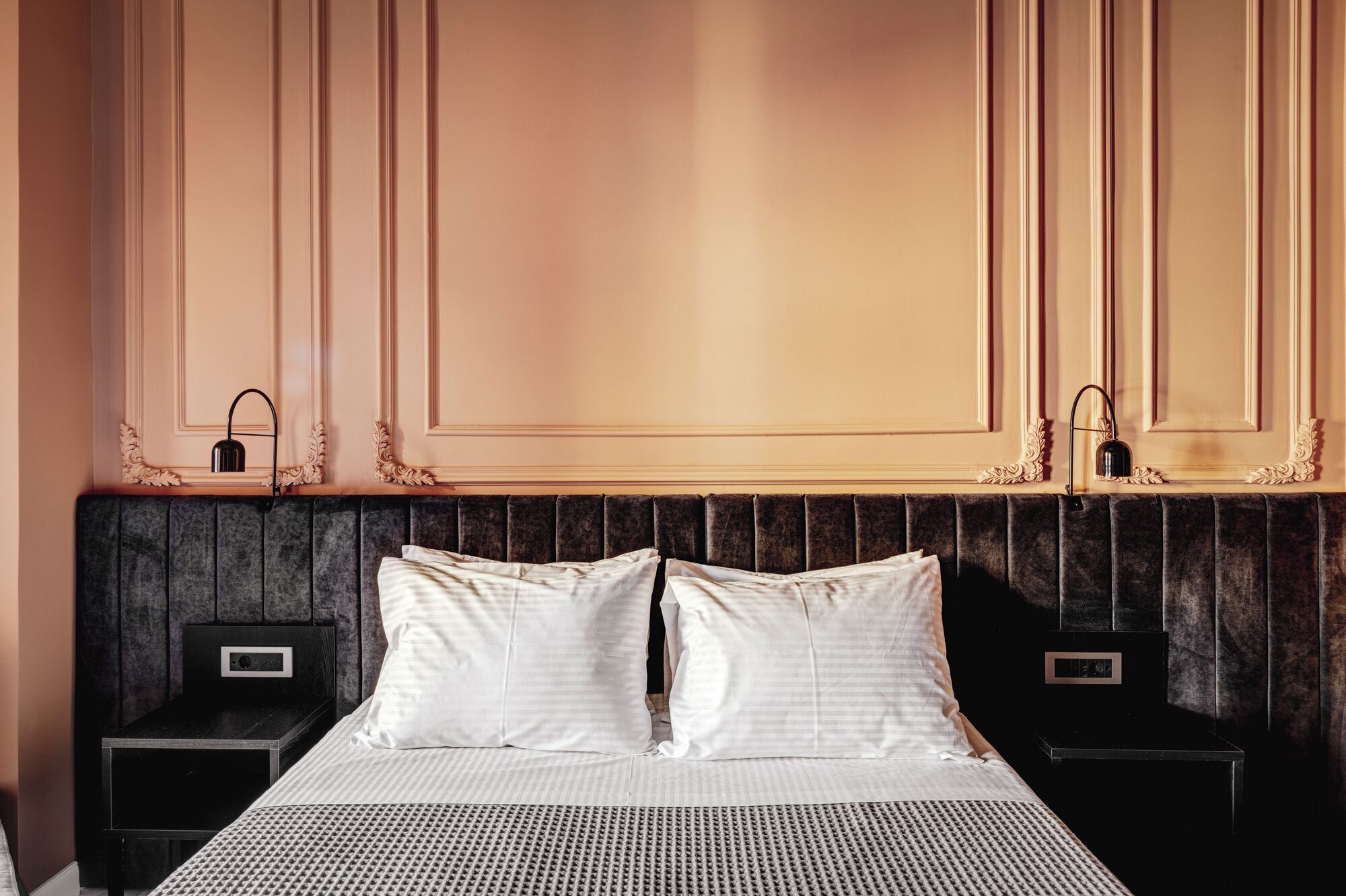 Hotelkamer met een groot bed, twee nachtkastjes, een hoofdeinde en een wand met decoratieve ornamenten.