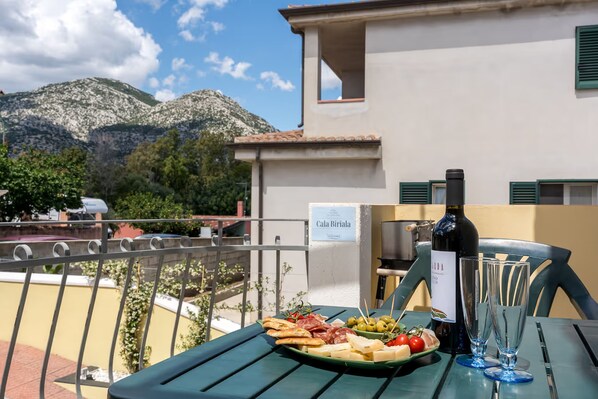 Eine Terrasse mit Tisch, gedeckt für eine Mahlzeit, einer Weinflasche und einem Schild mit der Aufschrift 'Cala Biriala'.