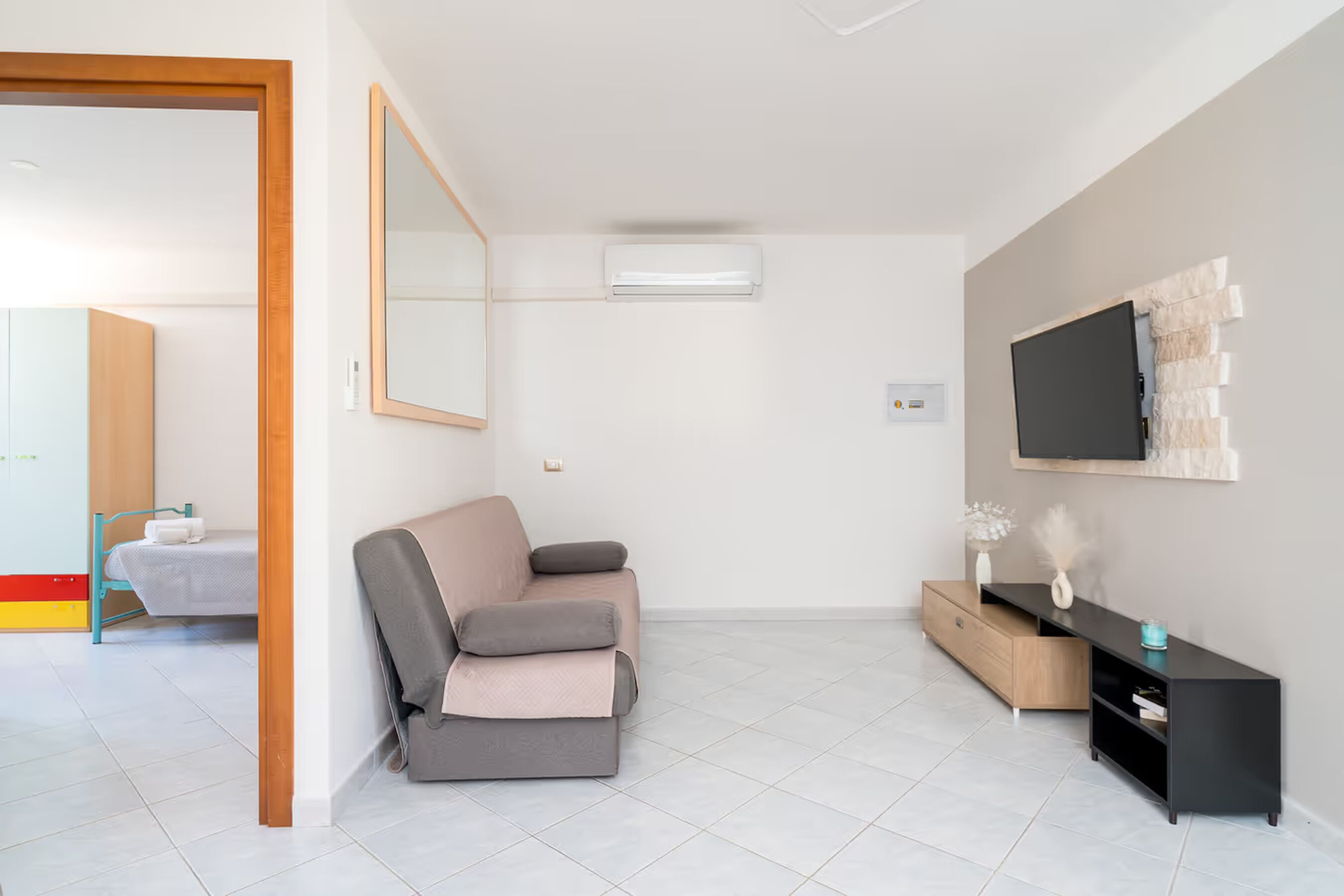 Uma sala de estar moderna com um sofá, uma televisão na parede, um armário de madeira e um aparelho de ar condicionado.
