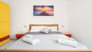 Ein Schlafzimmer mit einem hölzernen Bett, einem Nachttisch, einem gelben Kleiderschrank und einem Sonnenuntergangsbild an der Wand.